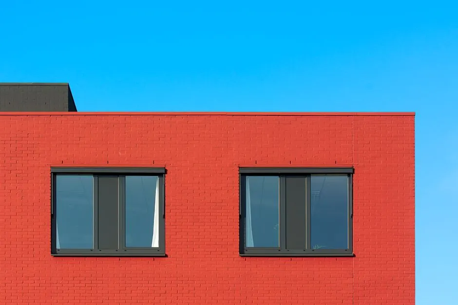 Photograph of a modern red brick building facade with two windows against a clear blue sky.
